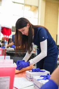 Female Nursing student practicing starting an IV on a simulated arm wearing gloves