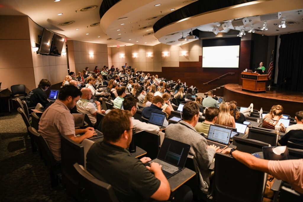 Many students sitting in large lecture hall at South College with laptops open