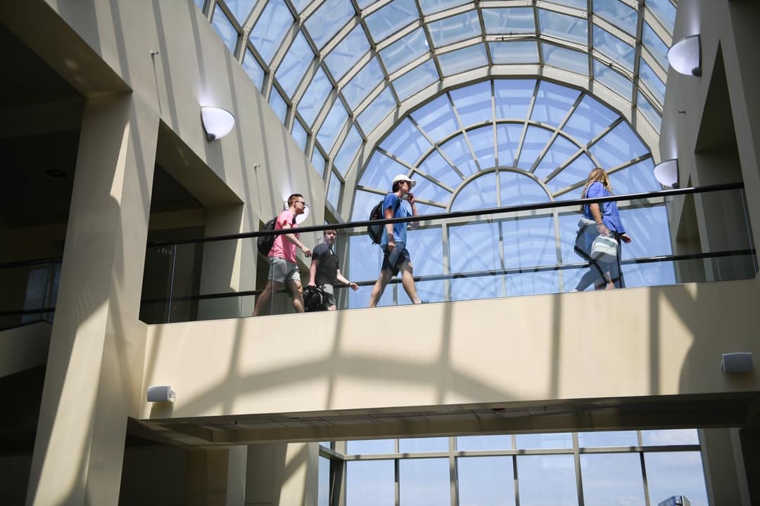 Large palladium window and elevated walking connector with 3 students going across.