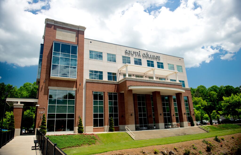 A modern, multi-story building with large windows and brick and white facades displays the sign "South College." Green trees and a blue sky surround the campus.